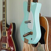 Close up of a collection of acoustic and electric guitars displayed on the wall